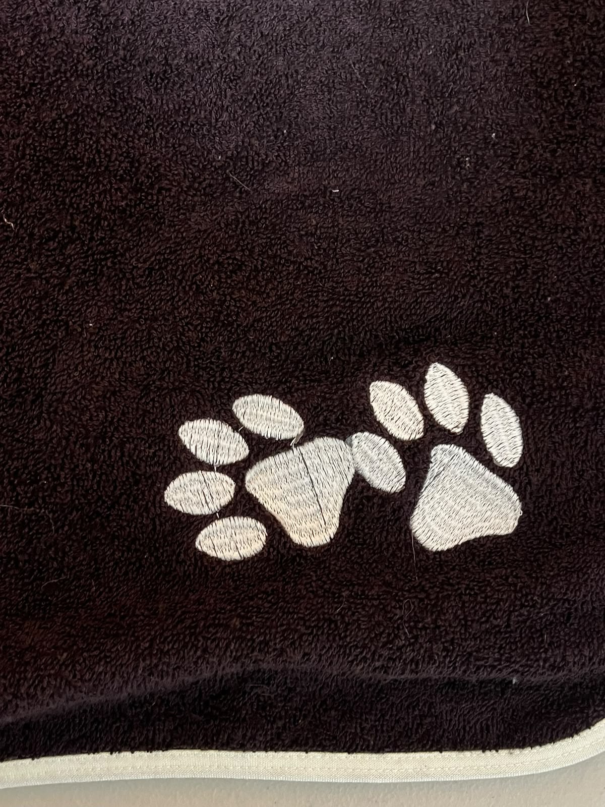 Acercamiento real del tejido café y el bordado de huellas blancas de Pet Towels