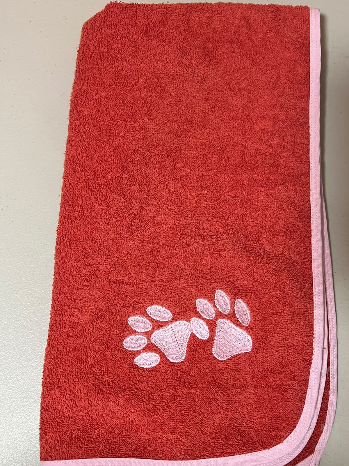 Pet Towels coral doblada con ribete rosa y bordado de huellas
