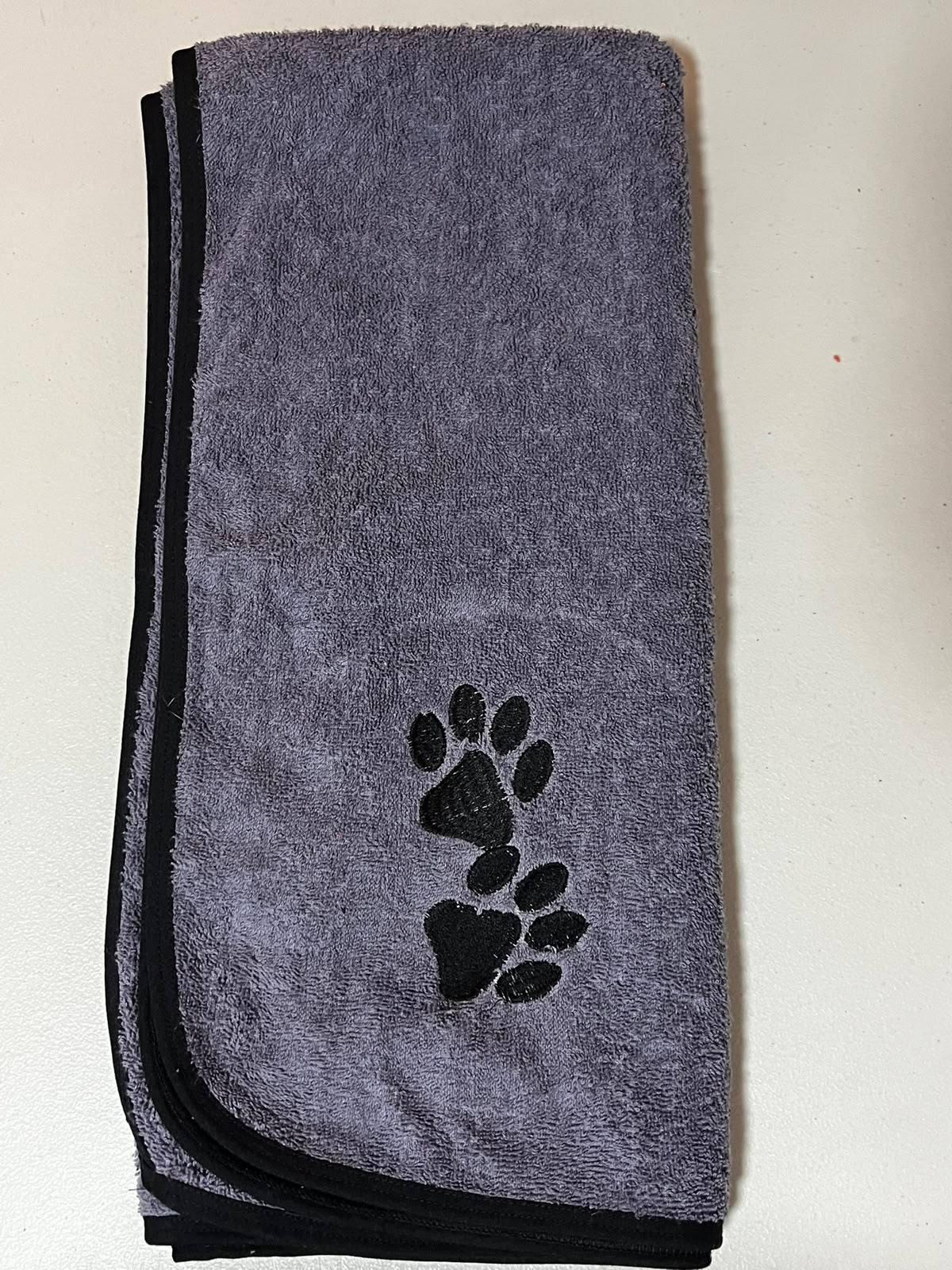 Pet Towels gris doblada con ribete negro y bordado de huellas