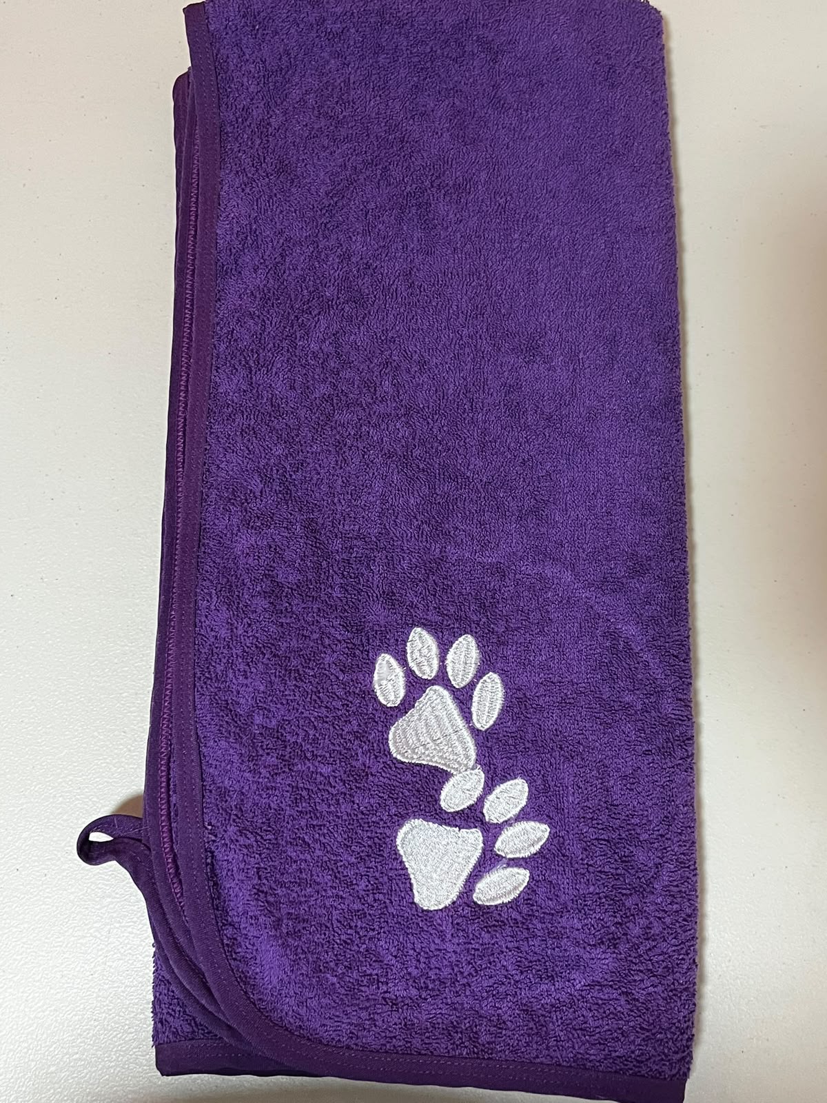 Pet Towels morada doblada con bordado de huellas blancas